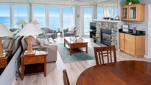 Ein großzügiges Wohnzimmer mit einem großen Fenster mit Blick auf das Meer, einem Kamin und einer Küchenzeile mit Holzausstattung.