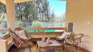 A balcony with wicker furniture, a table, and a view of trees and a fence. - Private villa with garden for two families !!100m from Solanas beach! 🏖 (Solanas)