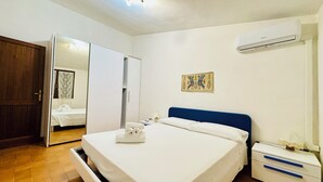 A bedroom with a bed, a nightstand, a wardrobe, and an air conditioning unit. - Private villa with garden for two families !!100m from Solanas beach! 🏖 (Solanas)