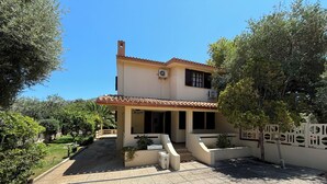A two-story house with a tiled roof, a covered patio, and a garden with various plants and a small pond. - Private villa with garden for two families !!100m from Solanas beach! 🏖 (Solanas)