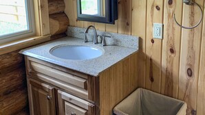 A wooden cabin bathroom with a sink, mirror, and two wall-mounted lights. - Cabins At Hay Creek Gorgeous Log Cabin Stunning Views of Glacier National Park (Polebridge)