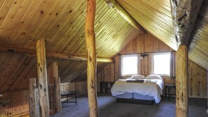 A cozy attic bedroom with a wooden ceiling, a bed, a bench, and a window. - Cabins At Hay Creek Gorgeous Log Cabin Stunning Views of Glacier National Park (Polebridge)