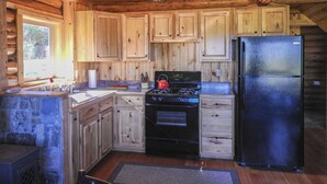 A wooden cabin kitchen with a stove, refrigerator, and wooden cabinets. - Cabins At Hay Creek Gorgeous Log Cabin Stunning Views of Glacier National Park (Polebridge)