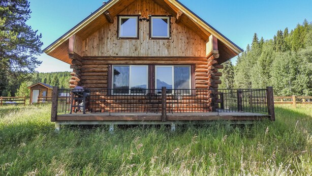 A log cabin with a deck and two large windows. - Cabins At Hay Creek Gorgeous Log Cabin Stunning Views of Glacier National Park (Polebridge)