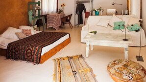 Een gezellige slaapkamer met een bed, een witte bank, een klein tafeltje en een stoel. Er is een kast, een lamp en een spiegel aan de muur.