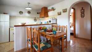 Een keuken met een houten tafel, stoelen, een koelkast, een magnetron en een spoelbak.