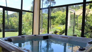 A hot tub with a wooden deck, surrounded by large windows offering a view of a lush garden and trees. - House / Villa - Aubenas (Aubenas)