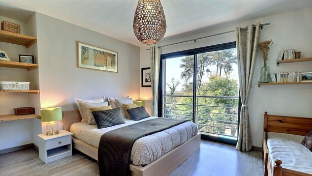 A modern bedroom with a large bed, bedside tables, a hanging light fixture, and a view of trees through the window. - House / Villa - Aubenas (Aubenas)