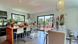 A modern kitchen with a central island, bar stools, and a dining area with a table set for four. - House / Villa - Aubenas (Aubenas)