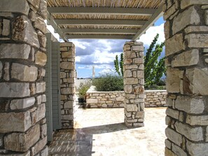 Relax on the covered patio surrounded by lush greenery and a stone wall.