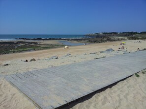 A beach with a wooden boardwalk leading to the shore, rocky areas, and a few people in the distance. - House / Villa - Batz sur Mer (Batz sur Mer)