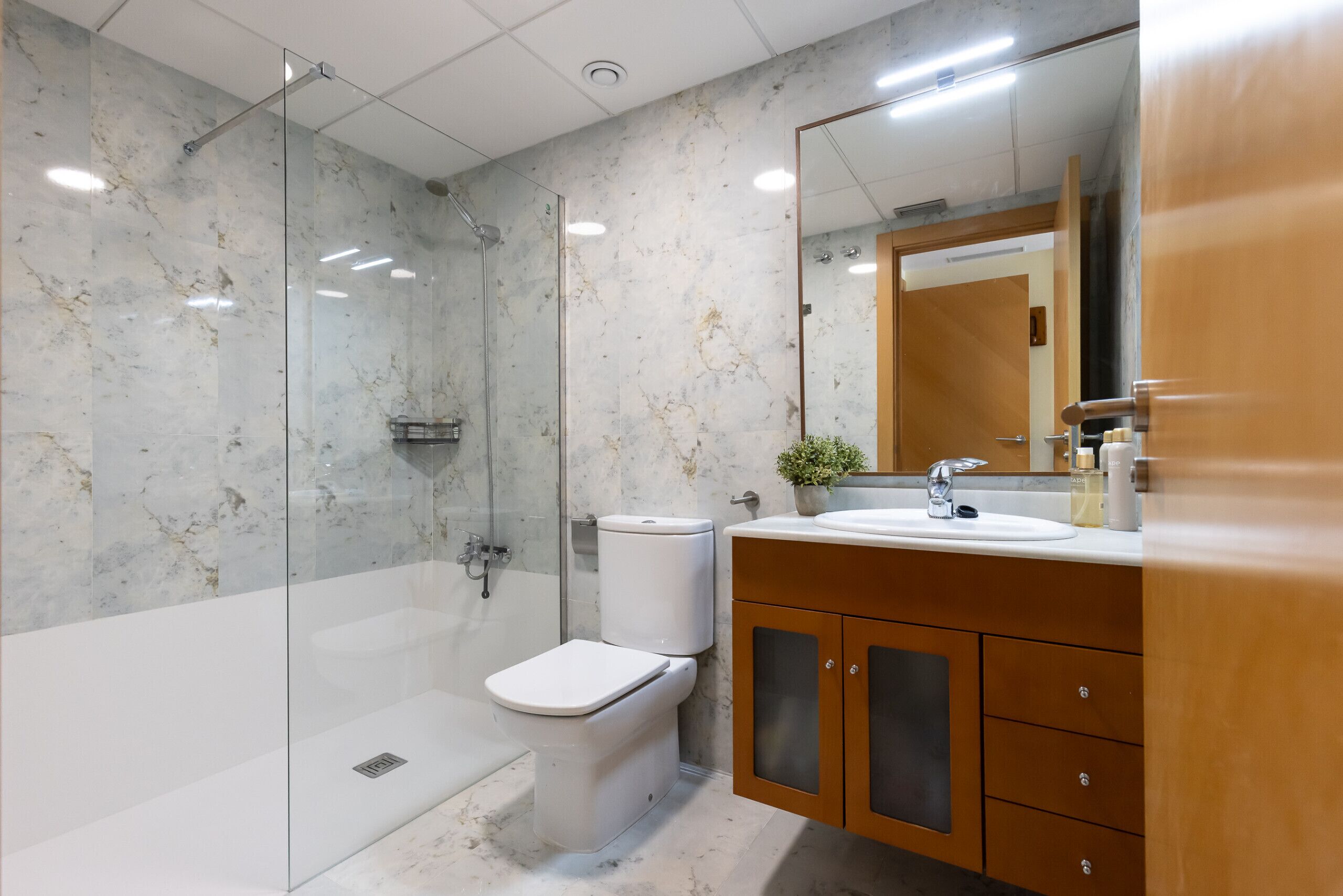 A modern bathroom with a glass-enclosed shower, a white toilet, and wooden cabinets.