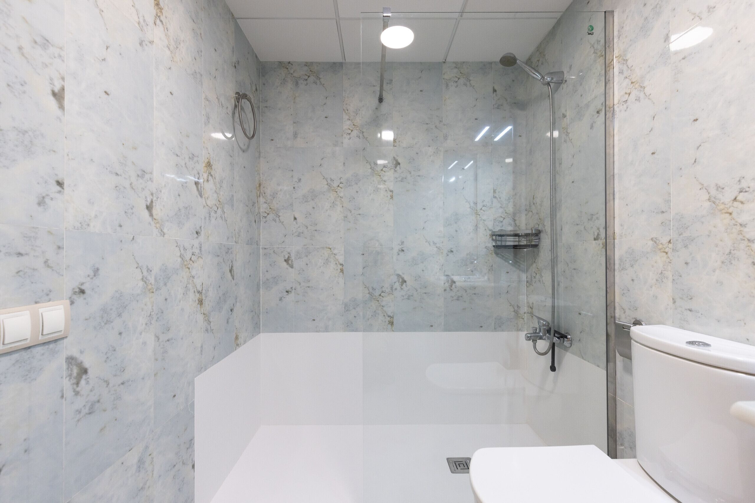 Een badkamer met een douchecabine van glas, een wit toilet en marmeren wanden.
