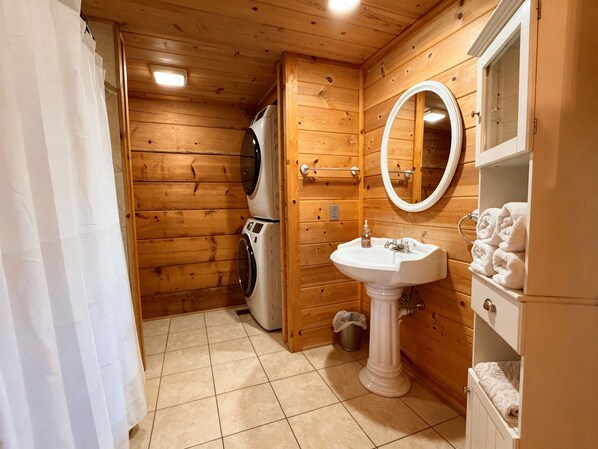 A wooden cabin bathroom with a washing machine, sink, and towel storage. - Romantic Couples Log Cabin #4 Hot Tub and Breathtaking Mountain Views near LURAY (Luray)