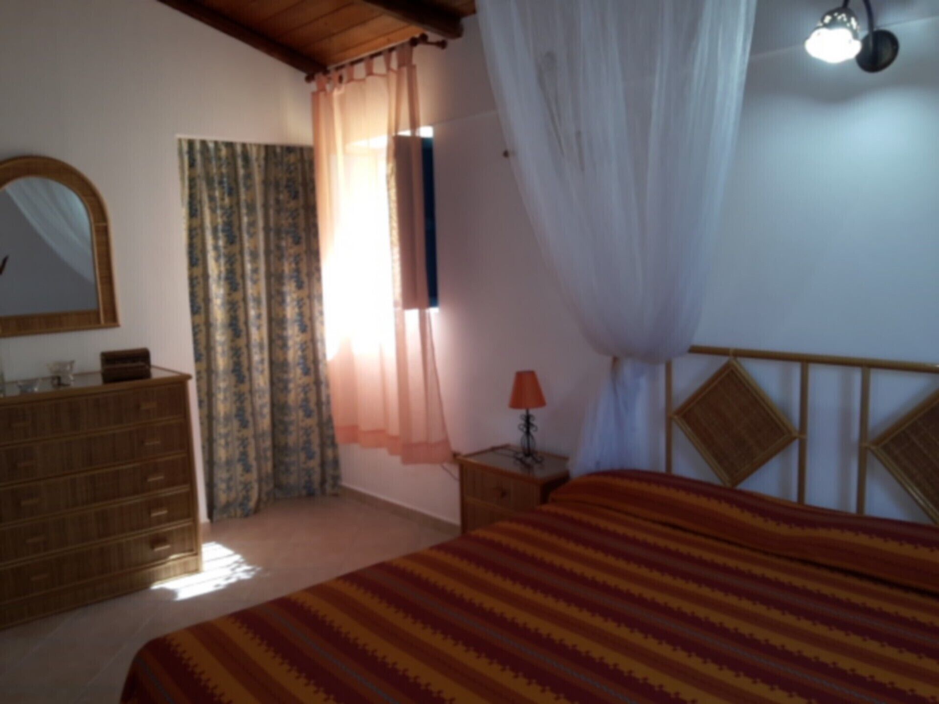 A bedroom with a bed, a dresser, a mirror, a lamp, and a window with curtains.