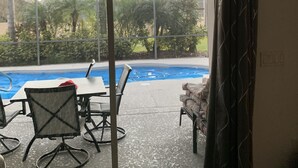 A room with a sliding glass door leading to a pool area, a ceiling fan, and a table with chairs. - Spacious, LUXURY 4 bedroom villa with pool and spa close to Disney (Haines City)