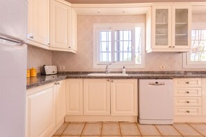 Una cocina con armarios blancos, lavavajillas, ventana con vistas y encimera con tostadora y cafetera.