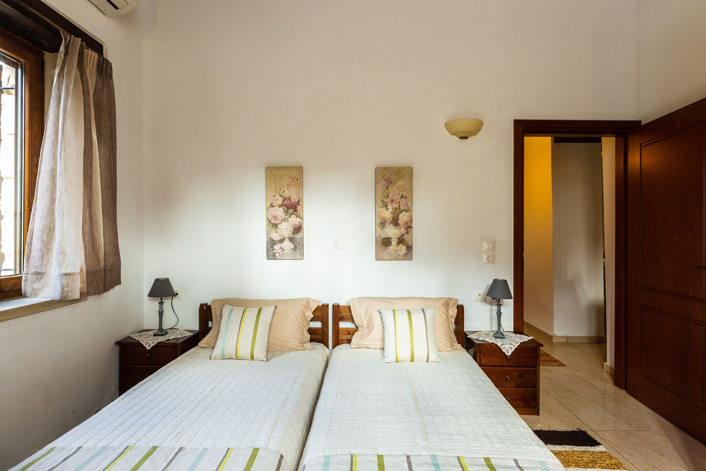 Ein Doppelbett mit zwei Nachttischen, ein Fenster mit Vorhängen und zwei an der Wand befestigte Gemälde.