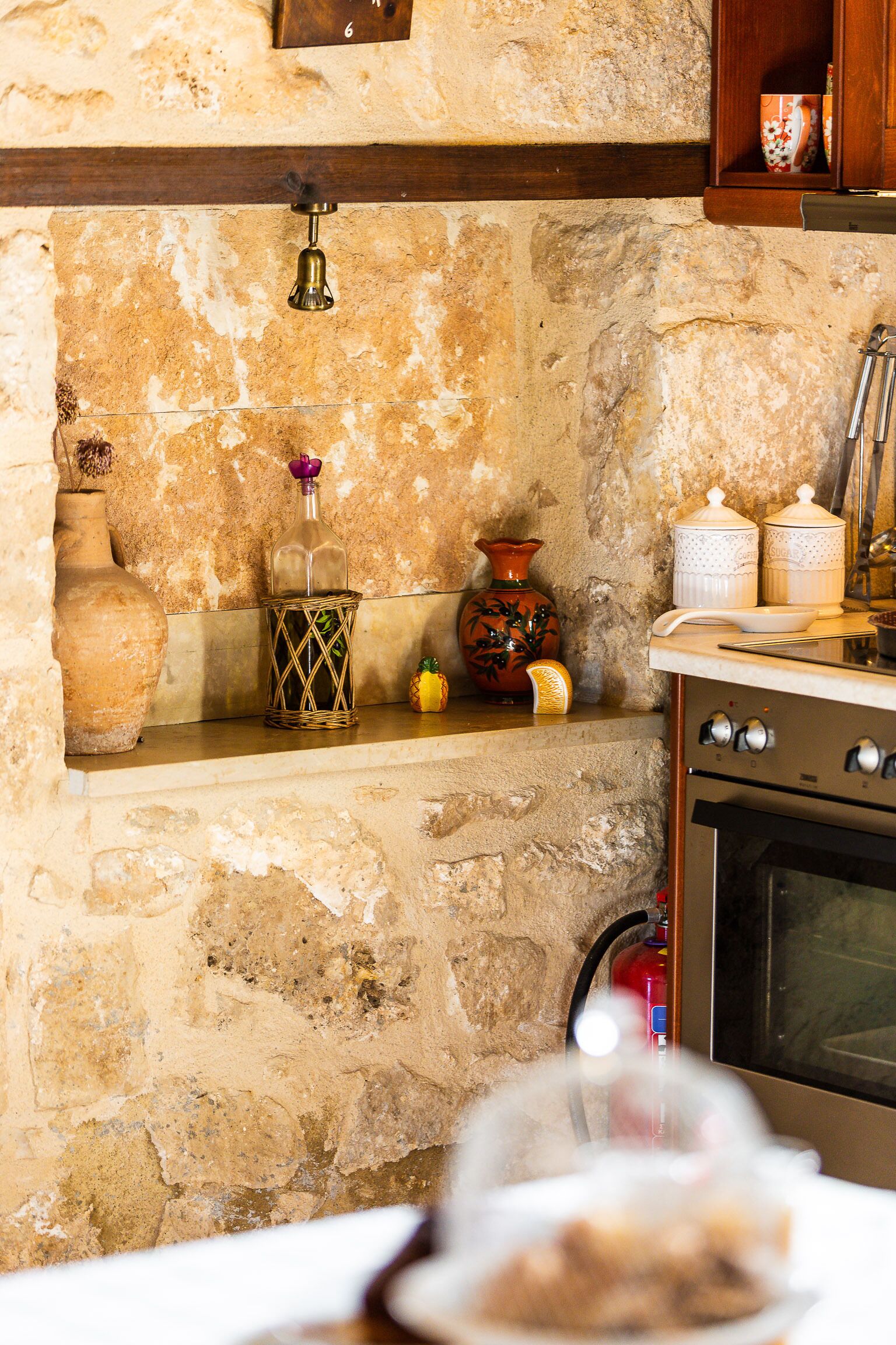 A kitchen with stone walls, a wooden shelf, and a stove.