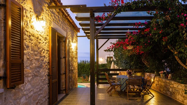 Ein Gebäude aus Stein mit Holzhinterfenstern, einer mit Blumen bewachsenen Pergola und einem Pool im Hintergrund.