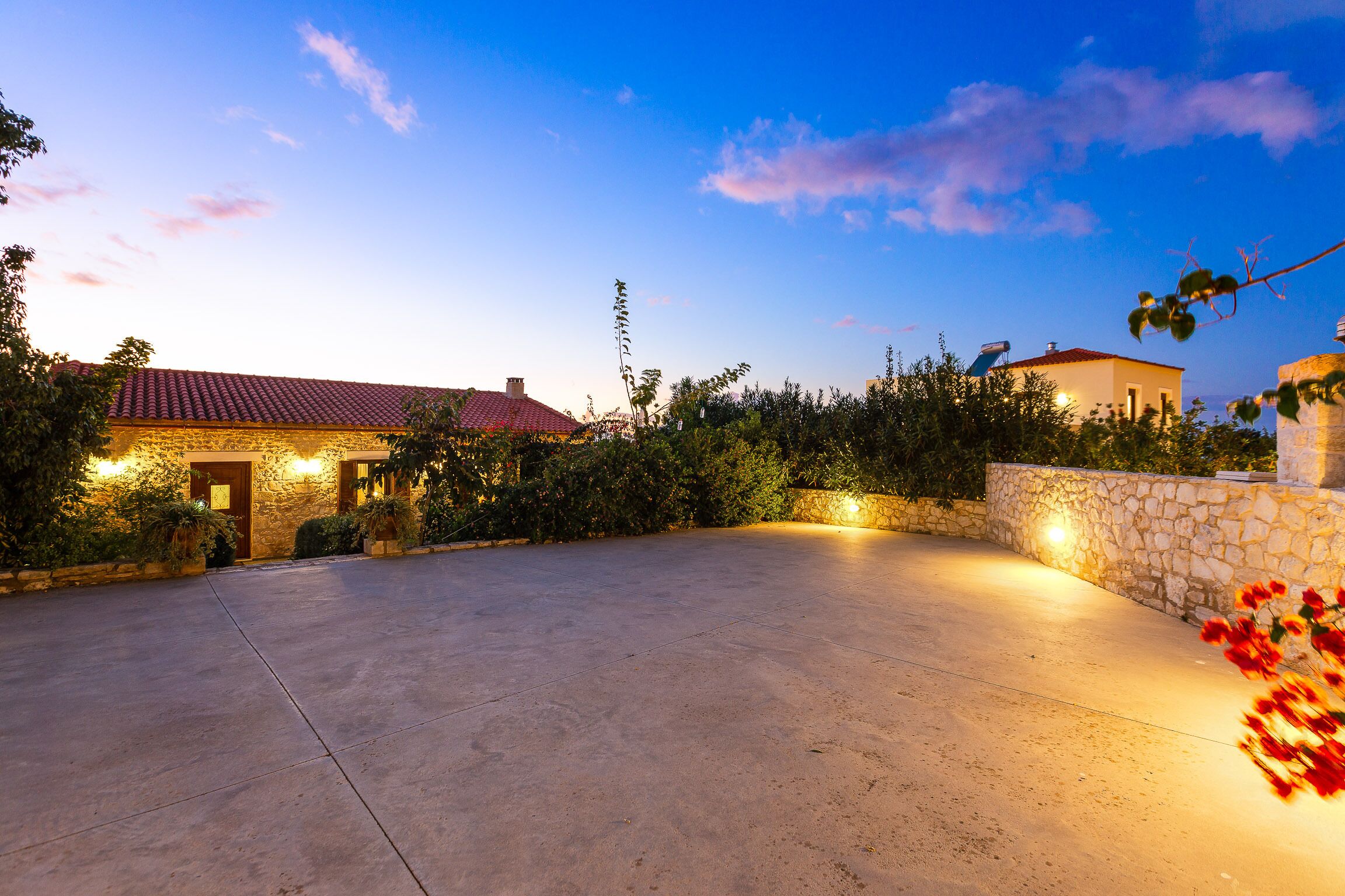 A spacious outdoor area with a stone wall and a building with a red-tiled roof.