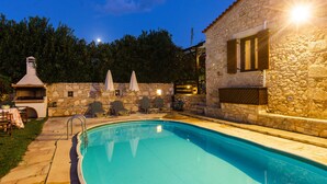 Ein Swimmingpool mit Steinmauern und einem Steinsschornstein, umgeben von Sitzgelegenheiten und Sonnenschirmen.