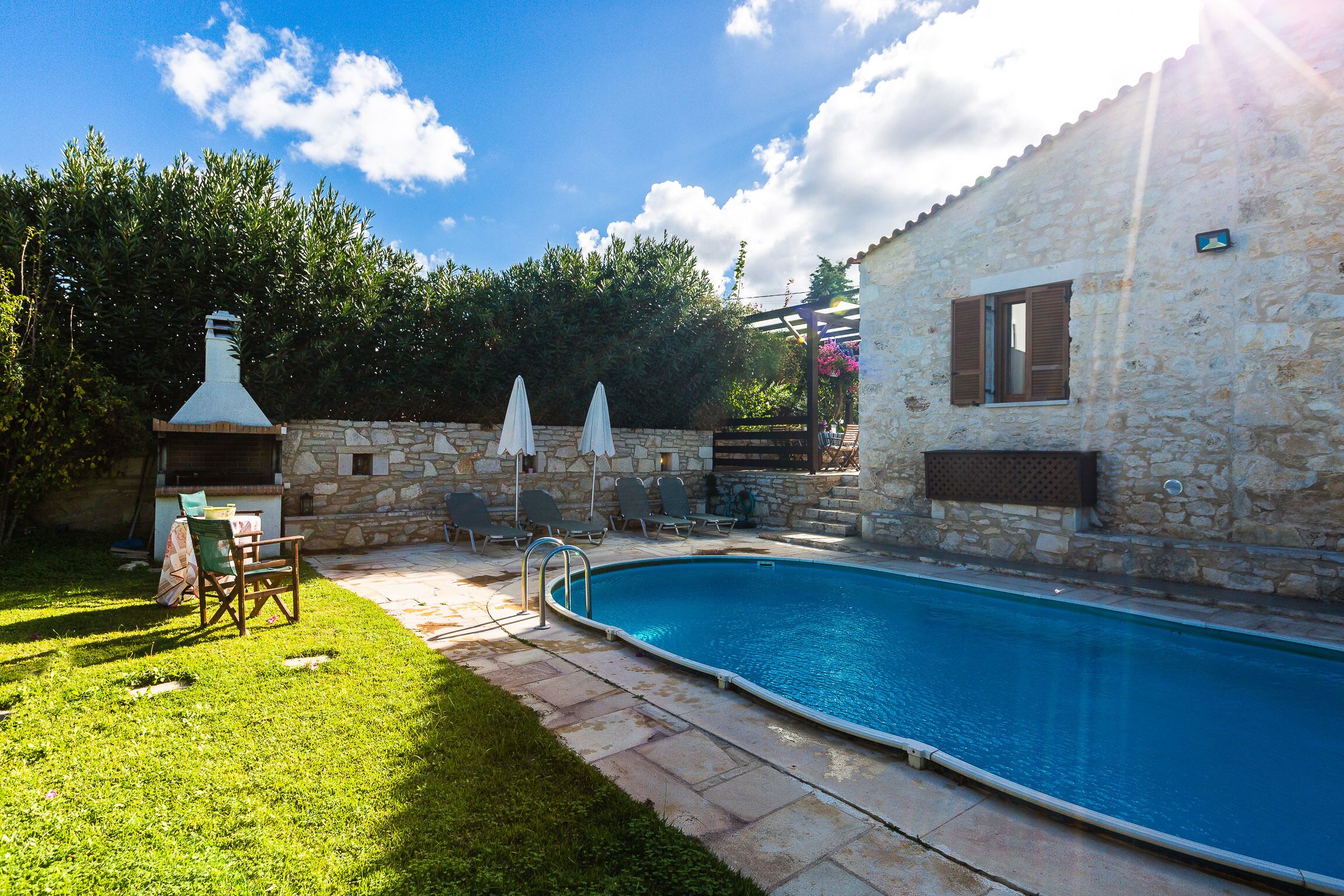 Une piscine avec un mur en pierre et une pergola ombragée par des parasols.