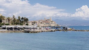 Une ville côtière dotée d’un château historique, d’un port de plaisance avec des bateaux et d’un quartier de restaurants agrémenté de parasols.