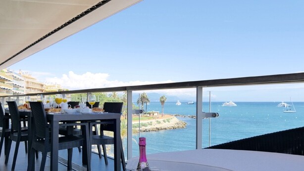 Un coin repas avec une table dressée pour deux personnes, donnant sur une marina où sont amarrés des bateaux.