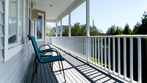 Een overdekt terras met witte relingen en een rij teal-kleurige stoelen.