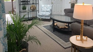 Een moderne woonkamer met een plafondventilator, een gestreept fauteuil, een ronde salontafel en een lamp.