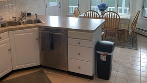 Een moderne keuken met witte kasten, een roestvrijstalen spoelbak en een eethoek met houten stoelen en een tafel.