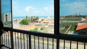 A view from a window overlooking a coastal area with buildings, a road, and a bus. - Apartment in Fortaleza, CE, Praia do Futuro, 3 bedrooms, 100m2 with 3 air conditioners, Wi-Fi. (Fortaleza)