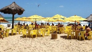 A beach with yellow chairs and umbrellas, a thatched umbrella, and a person kite surfing in the background. - Apartment in Fortaleza, CE, Praia do Futuro, 3 bedrooms, 100m2 with 3 air conditioners, Wi-Fi. (Fortaleza)