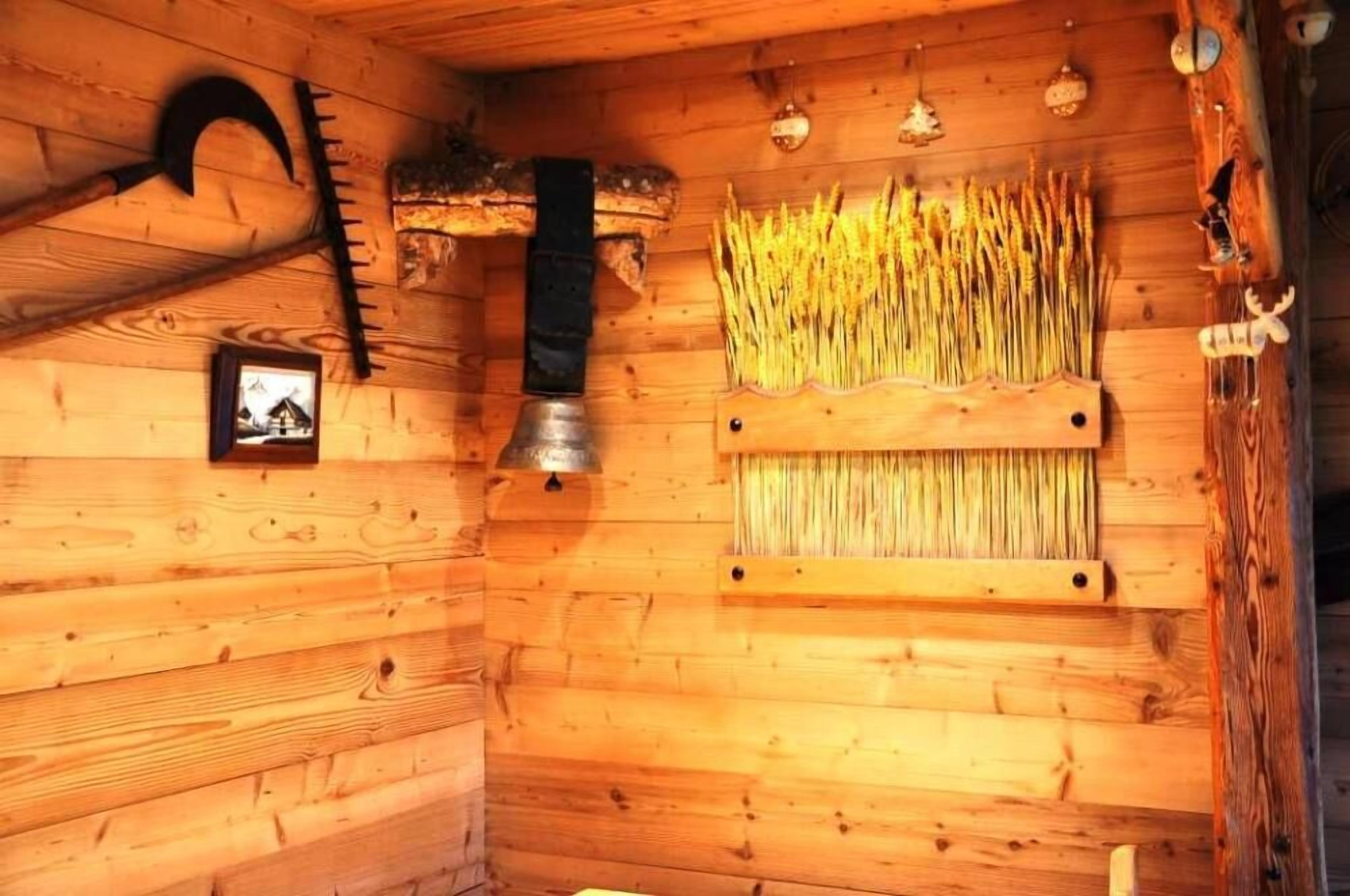 L’intérieur d’un chalet en bois, au style rustique, présente un mur en bois orné d’un tableau encadré, une cloche en métal et une étagère avec des plantes séchées.