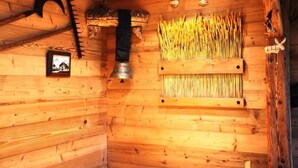 Interieur van een houten chalet met een rustieke uitstraling, met een houten wand met een ingelijste foto, een metalen bel en een plankje met gedroogde planten.