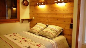Een gezellige kamer met een houten hoofdbord, een bed met beddengoed met een patroon, een hangende koperen pan en een klein plankje met decoratieve objecten.