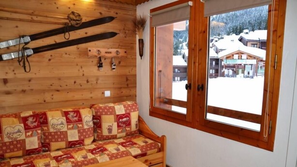 Een houten hut interieur met een bank, ski's en een raam met uitzicht op een besneeerd landschap.