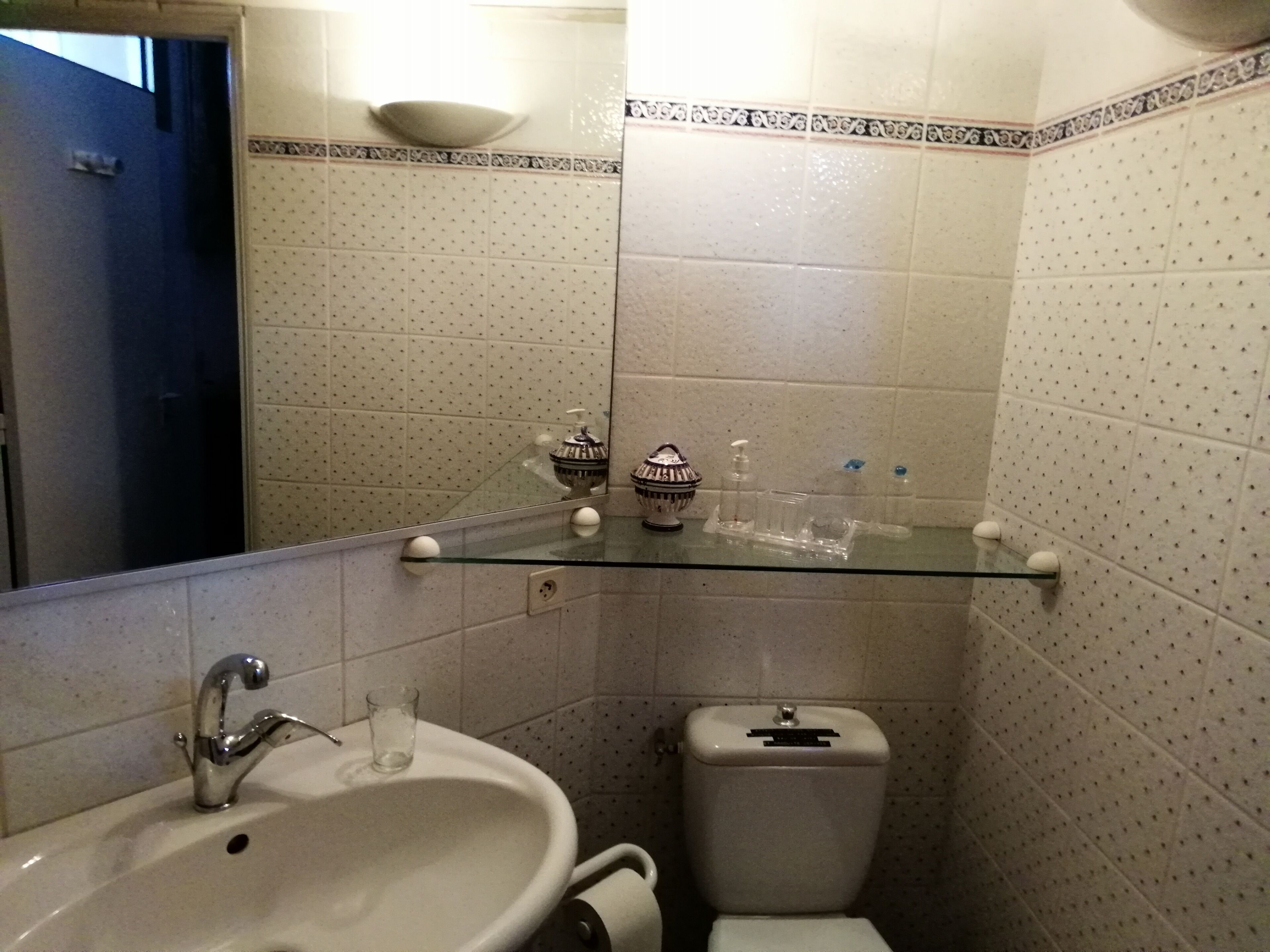 Een badkamer met een wastafel, spiegel, toilet en een glazen plank met toiletartikelen.