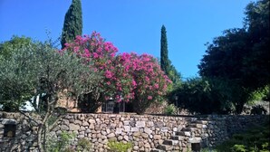 A stone wall with a building partially visible behind it, surrounded by trees and a clear blue sky. - Holiday Gite in Southern Ardeche (Joyeuse)