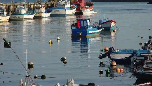 Un puerto con varias embarcaciones amarradas, un faro al fondo y aguas tranquilas.