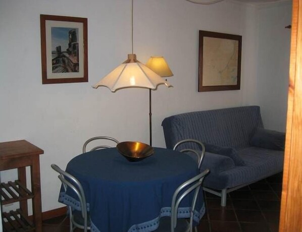 A dining area with a round table, chairs, a bowl, a lamp, and a sofa. - CASA SÃO JOÃO T1 - 1 bedroom apartment 100 m from the beach (Peniche)
