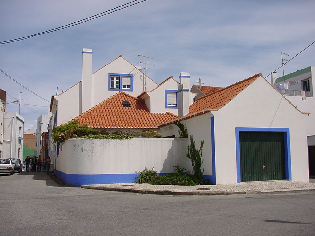 A residential street with houses featuring red-tiled roofs and blue-framed windows.
