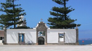 Una iglesia pequeña de color blanco con un campanario, una bicicleta estacionada adelante, y una señal de stop al fondo.