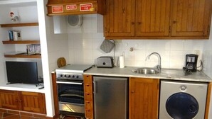Una cocina compacta con armarios de madera, horno empotrado, lavavajillas y cafetera.