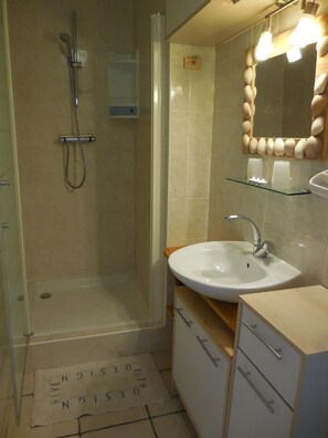 A bathroom with a glass shower enclosure, a white sink, and a mirror with a decorative frame.
