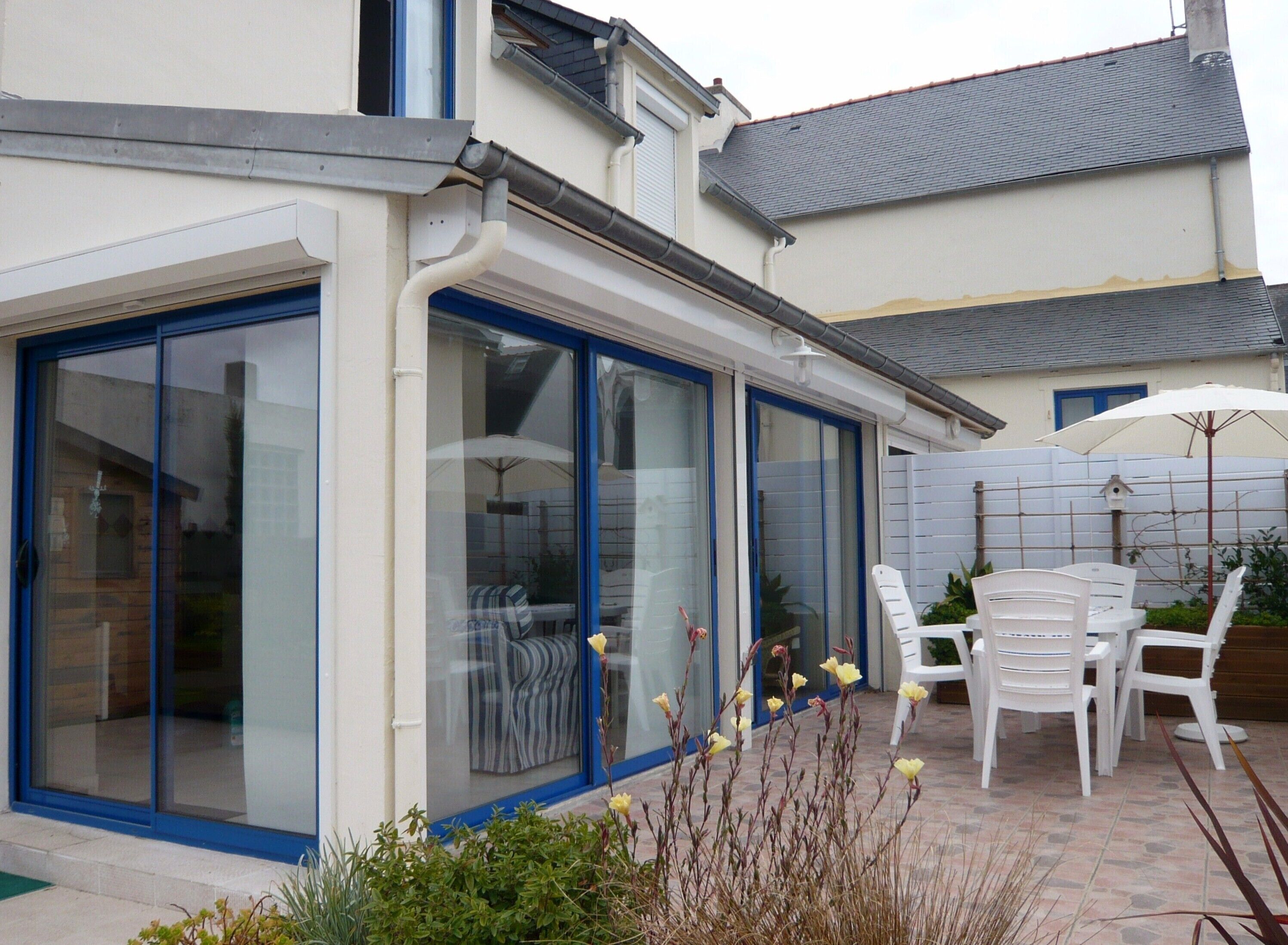 Et hus med store skydedøre, en terrasse med hvide plastikstole og en hvid parasol.