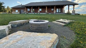 A modern building with a stone facade, a covered porch, and a fire pit in the foreground. - Cozy Cabin | 20 MI to YNP | Walk to Henry’s Lake (Island Park)
