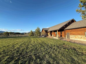 Un chalet rustique, doté de fondations en pierre et d’une façade en bois, situé dans un champ verdoyant avec des montagnes en toile de fond.