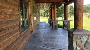 A covered wooden porch with stone pillars, leading to a grassy area. - Cozy Cabin | 20 MI to YNP | Walk to Henry’s Lake (Island Park)